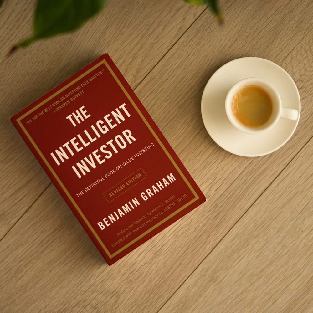 O livro O Investidor Inteligente, de Benjamin Graham, sobre uma mesa de madeira ao lado de uma xícara de café
